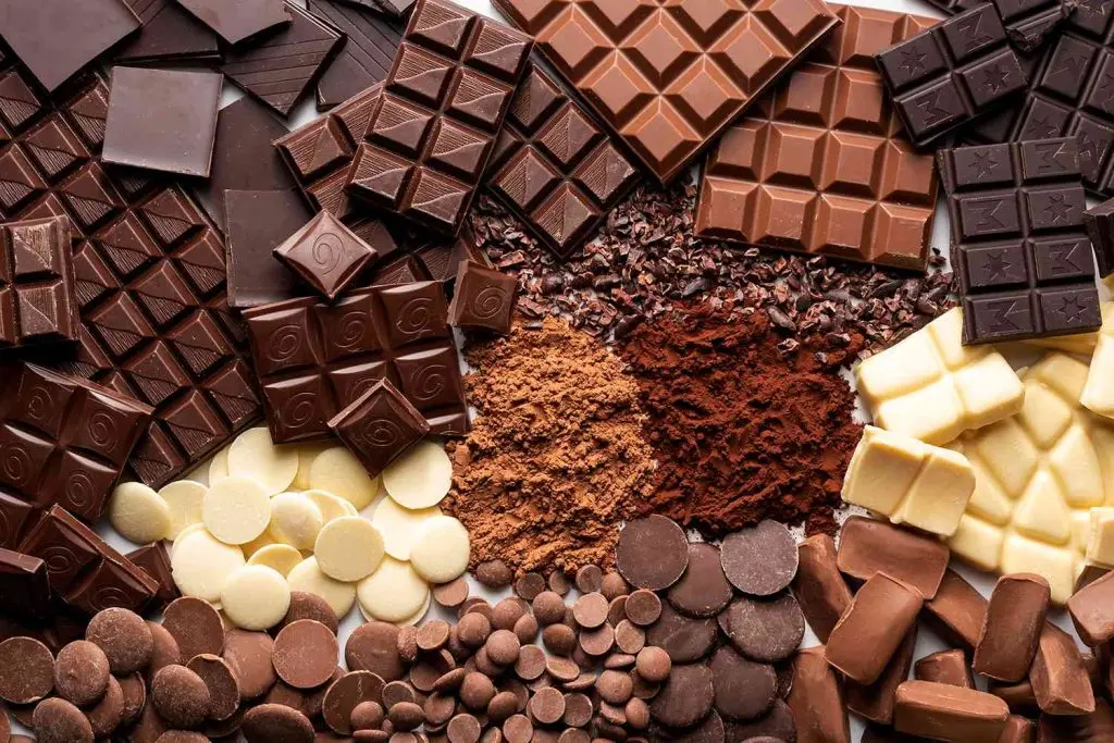 چند نوع شکلات در یک سبد چوبی با برگ‌های کاکائو اطراف