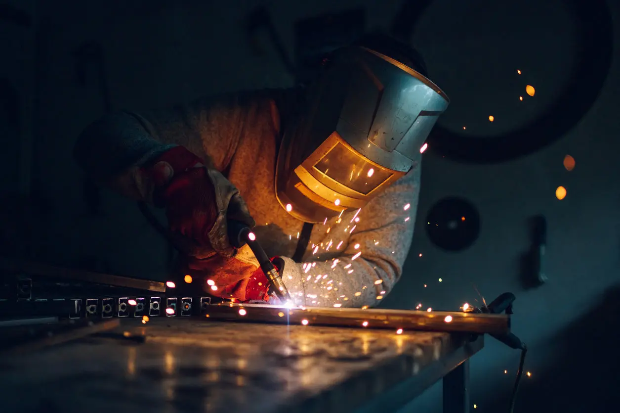 یک جوشکار حرفه‌ای در حال بررسی کیفیت جوشکاری روی یک قطعه فلزی بزرگ